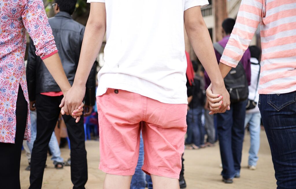 A person wearing a white shirt and pink shorts stands in the middle of the picture, while their hands are being held either side. There is a crowd of people ahead of them.