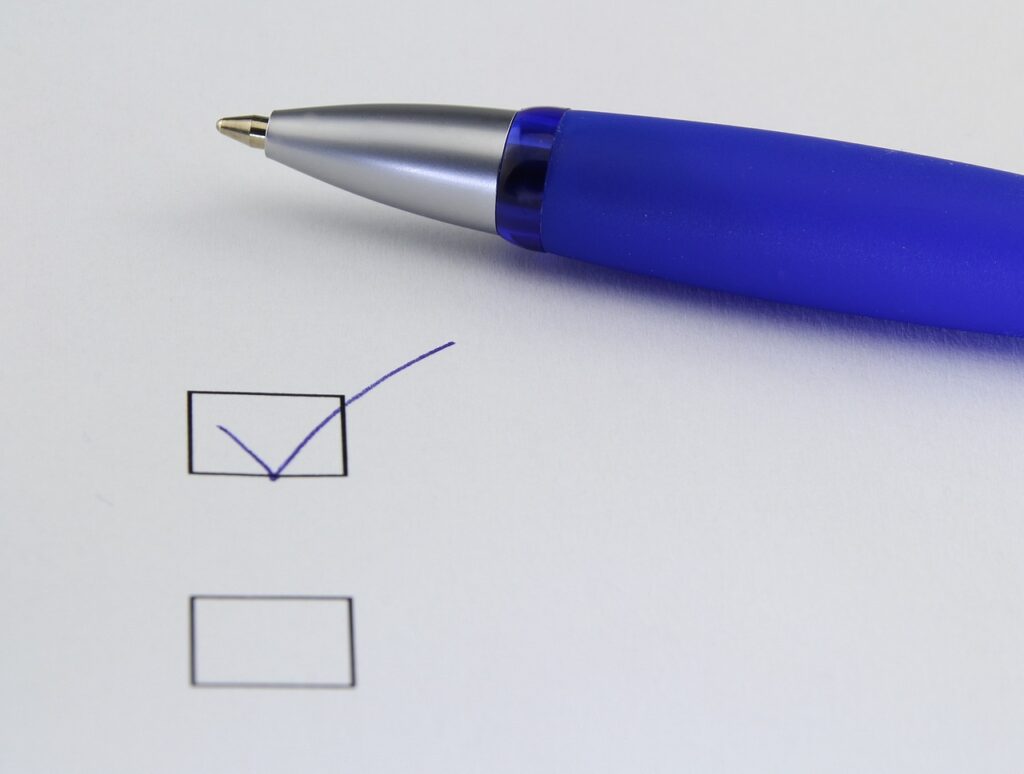 Two checkboxes are seen on a piece of white paper, one ticked with blue ink, while the other is empty. A blue coloured plastic pen is visible lying on above the checkboxes.