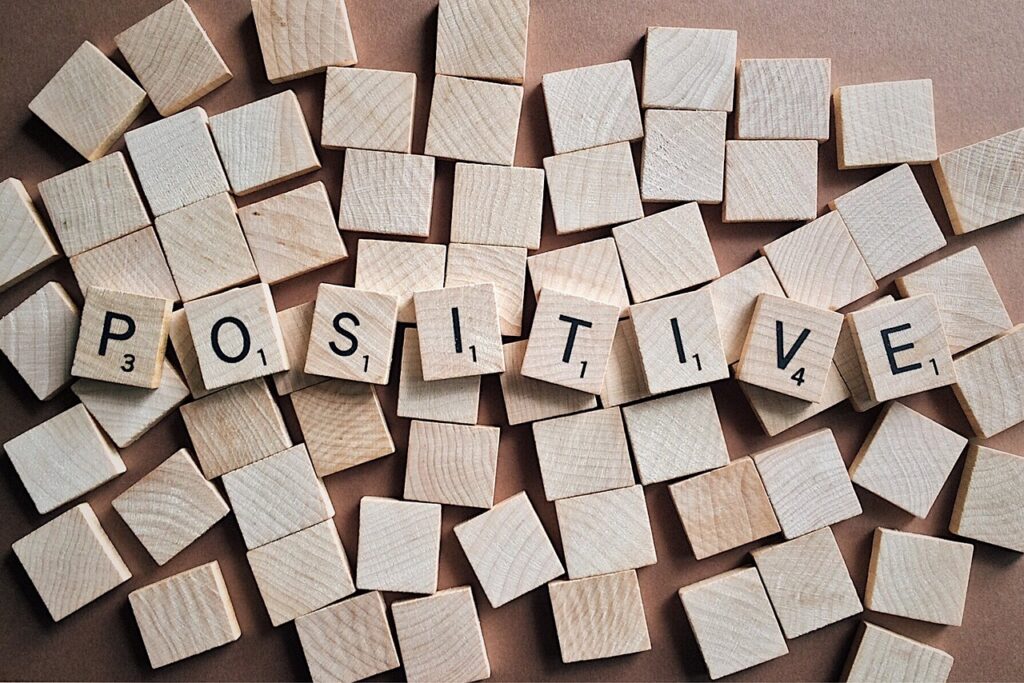 The word "positive" is spelled out by wooden blocks, and these blocks are spread out on top of a bottom of layer of blank wooden square blocks. 